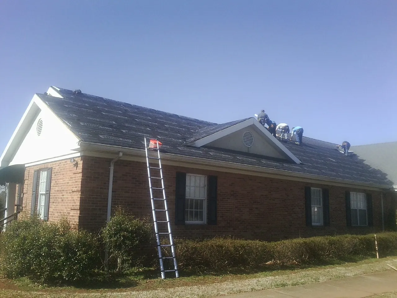 Crew tearing shingles off a brick ranch roof with a ladder set — Metal Roof Repair work by our crew in Dover Plains