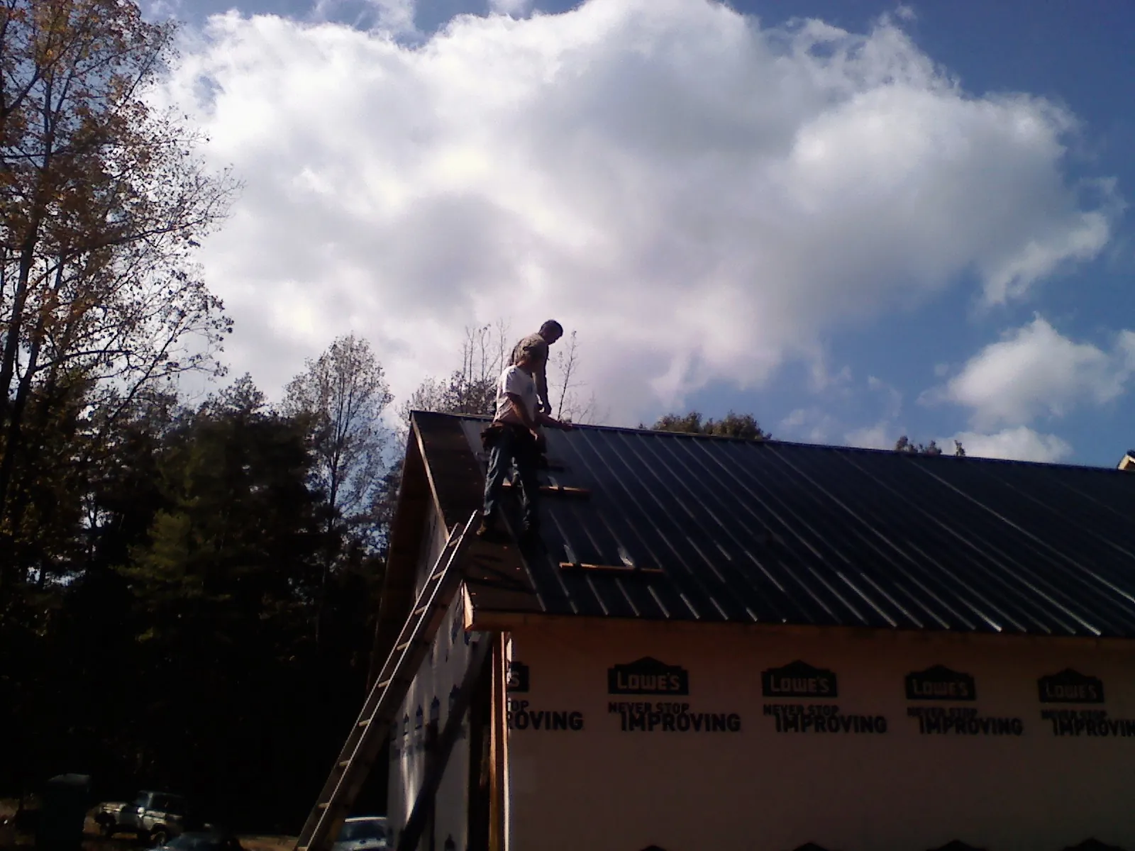 Roofer fastening dark metal panels high against a cloudy sky, from a Roof Inspection job in Dover Plains