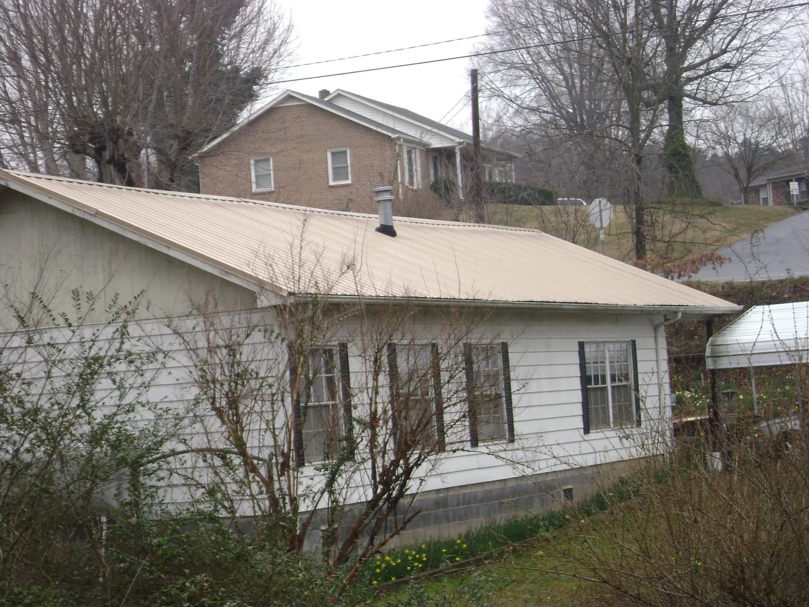 Tan metal roof on a white sided house set into a hillside — Commercial Roofing by Roofing Brothers in Dover Plains